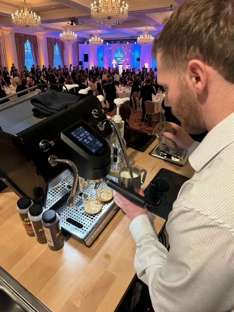 Barista working a mobile coffee bar inside a ballroom gala with chandeliers